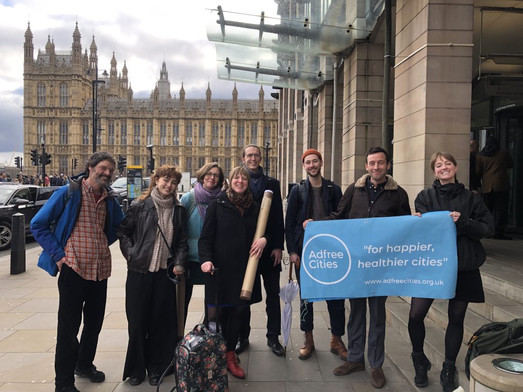 A group of 8 people stand on the street holding a banner that reads "adfree cities"