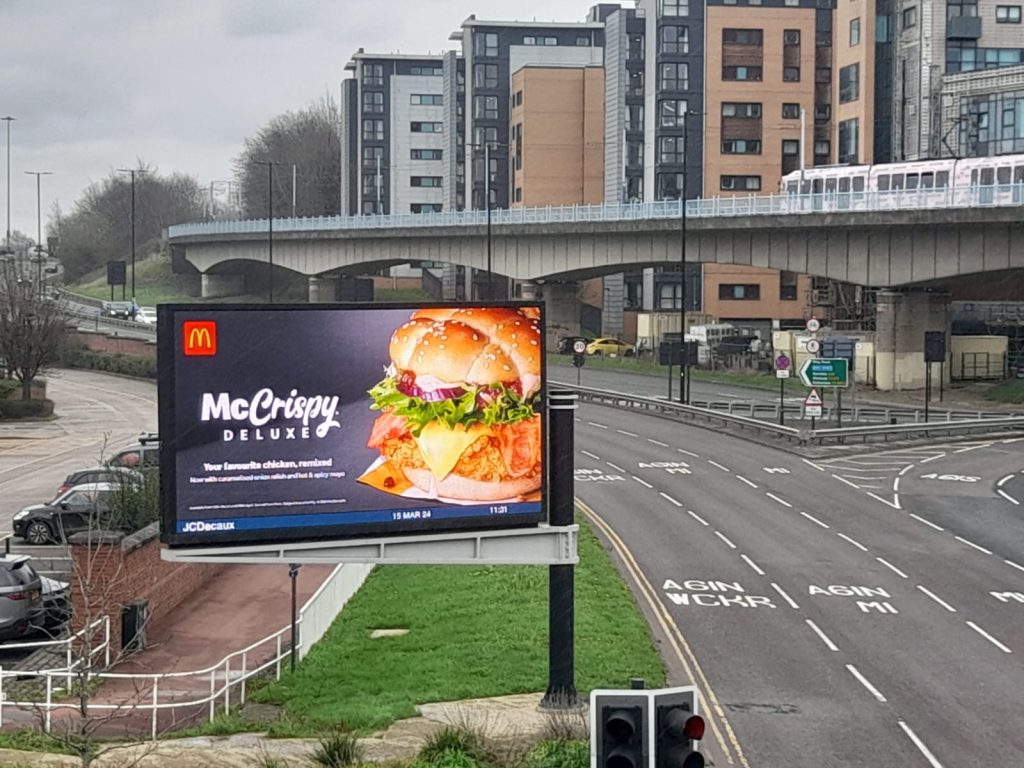 A large digital billboard above a road displays an ad for McDonald's
